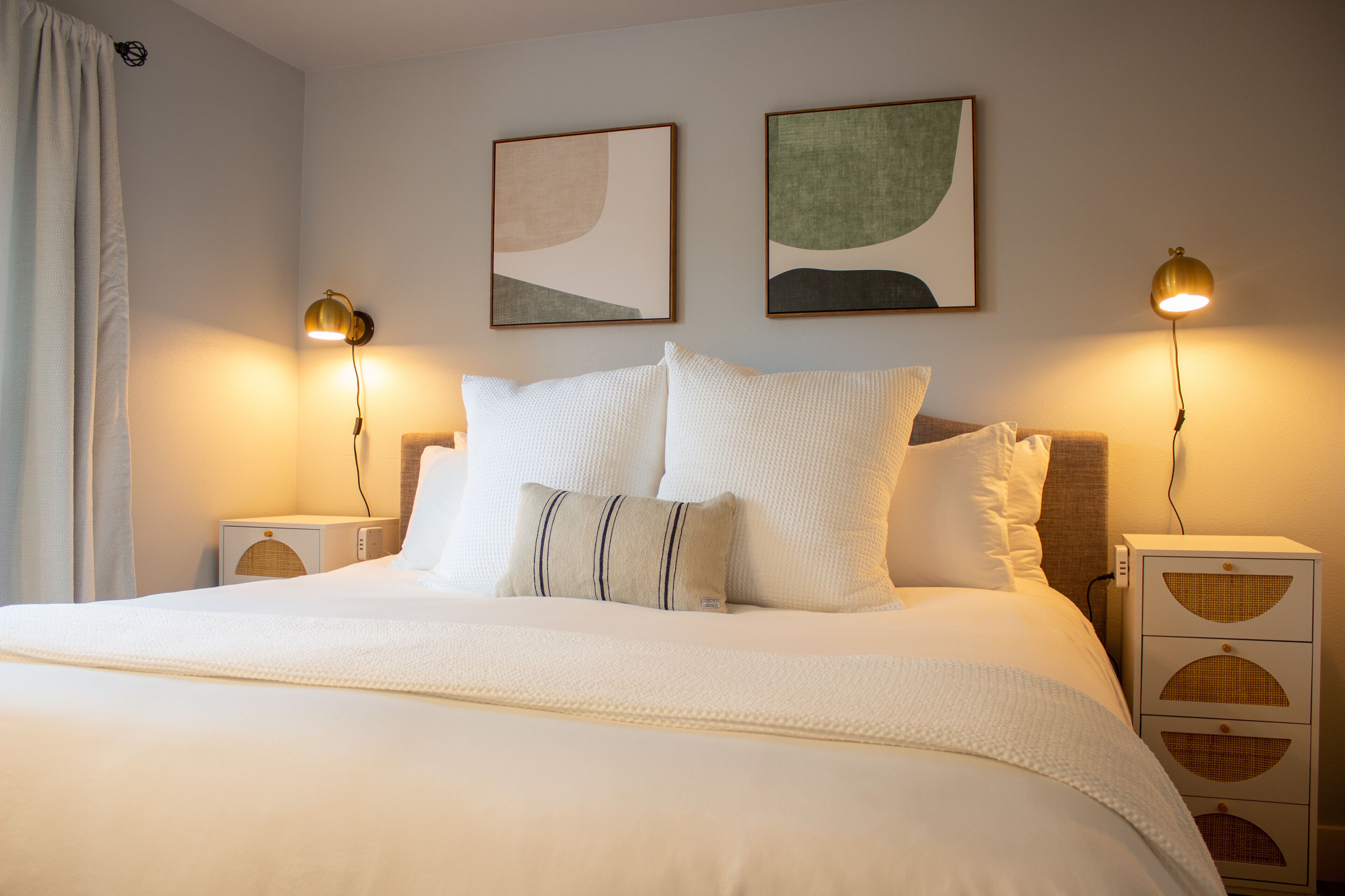 A neatly made bed with white bedding and two pillows, flanked by bedside tables with lamps.