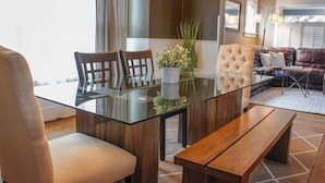 Un salon moderne avec une table à manger à plateau de verre, des chaises en bois, un canapé et une table basse.
