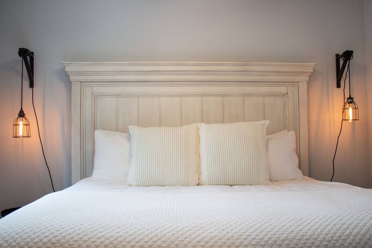 A neatly made bed with a white headboard and two wall-mounted light fixtures on either side.