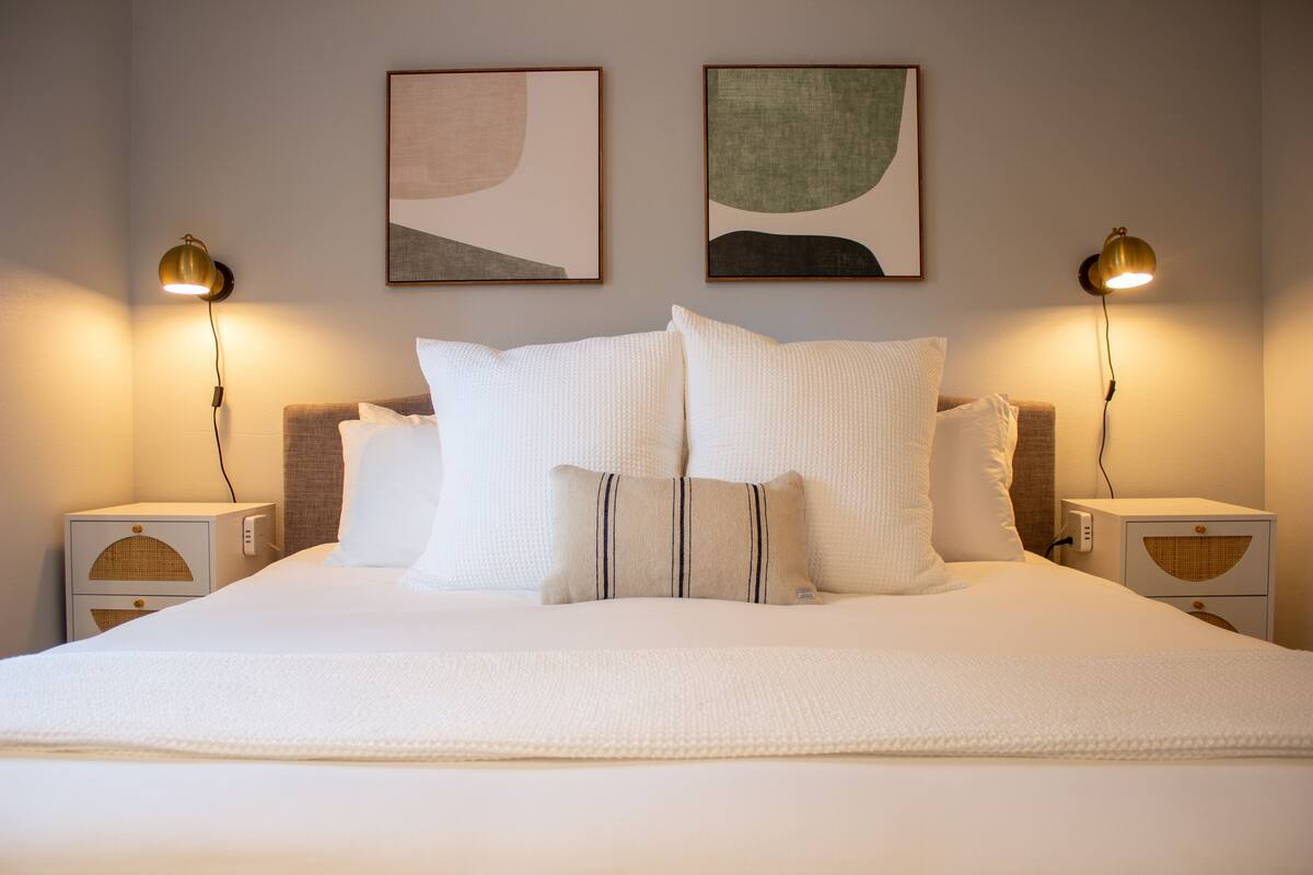 A neatly made bed with white bedding and two wall-mounted lamps on either side.