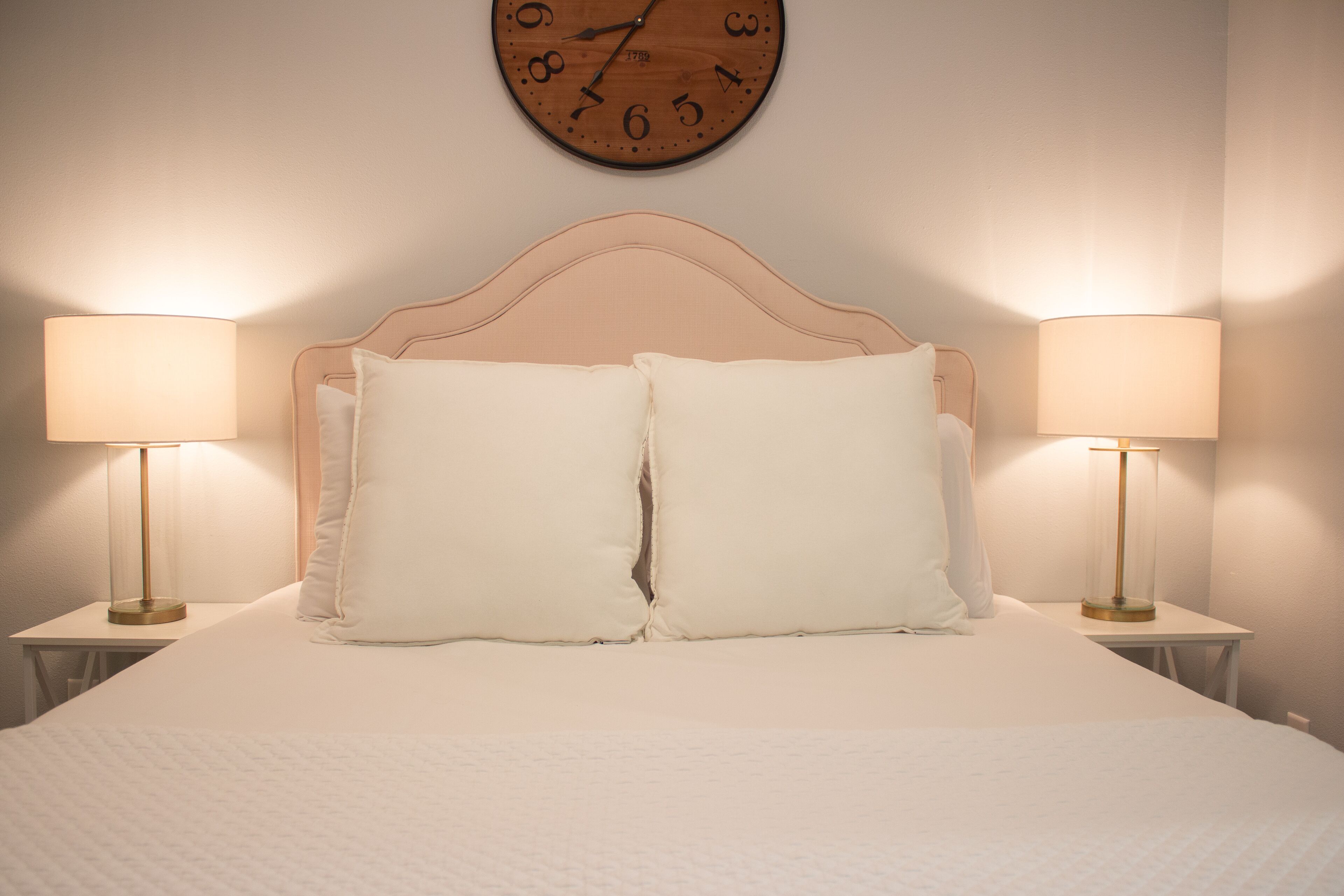 Una cama bien tendida con dos almohadas, un cabecero de madera y dos lámparas de noche a cada lado.