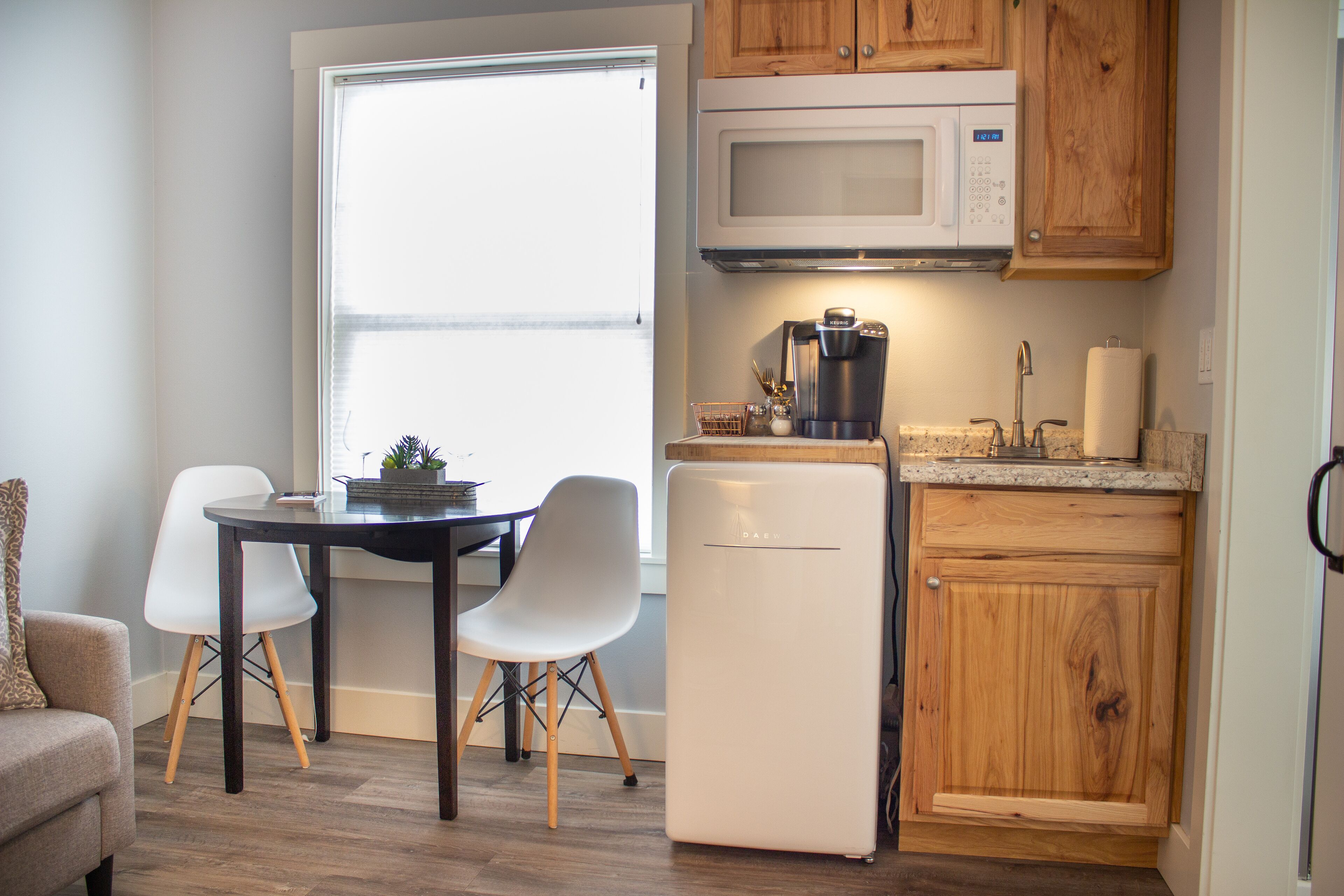 A compact kitchen with a microwave, coffee maker, and dishwasher. There is a dining table with two chairs and a small sofa in the corner.