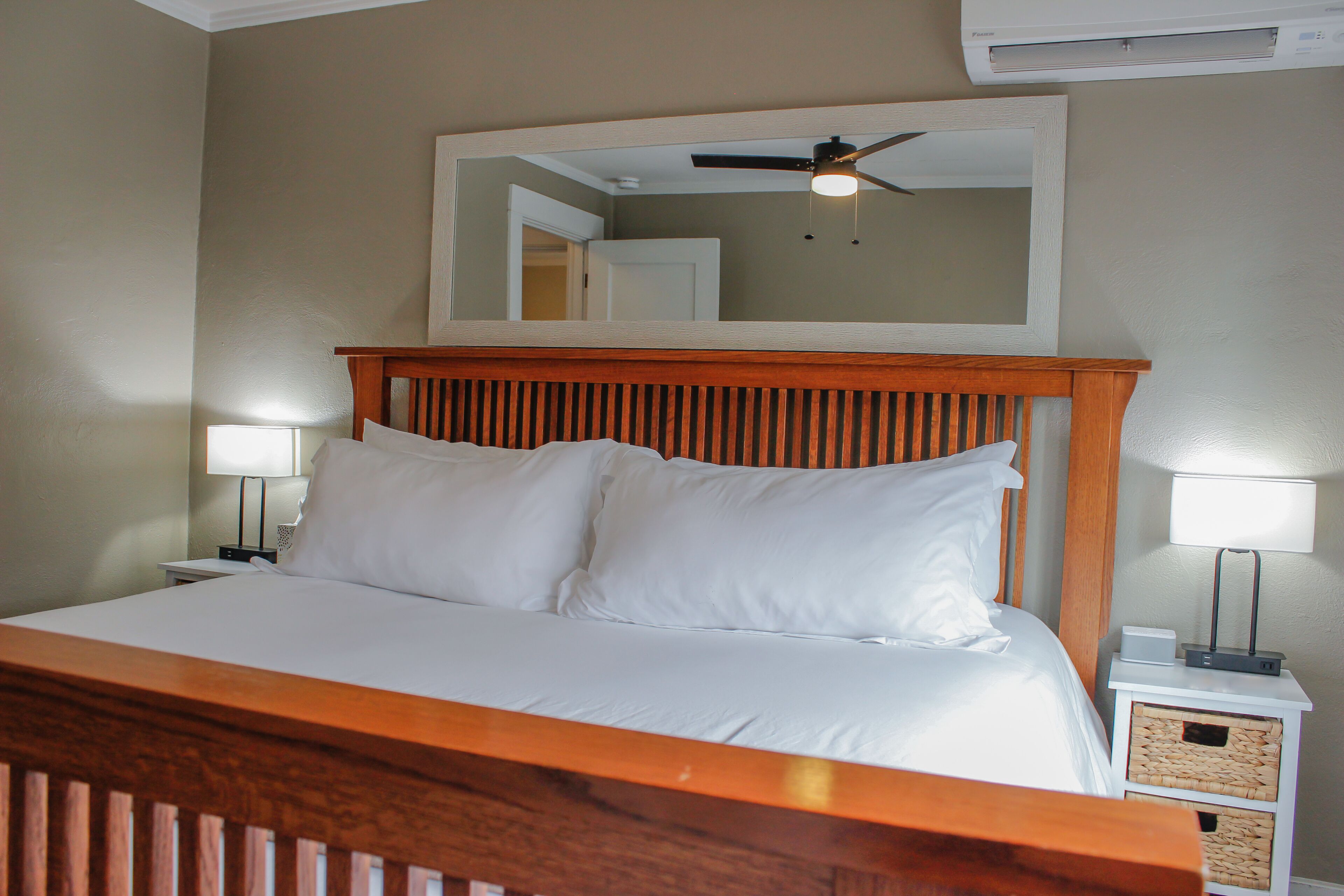 A neatly made bed with white linens, a wooden headboard, and two bedside lamps.