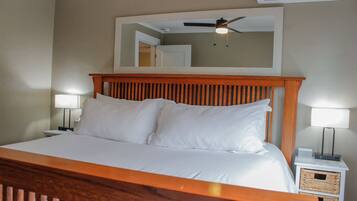 A neatly made bed with white linens, a wooden headboard, and two bedside lamps.