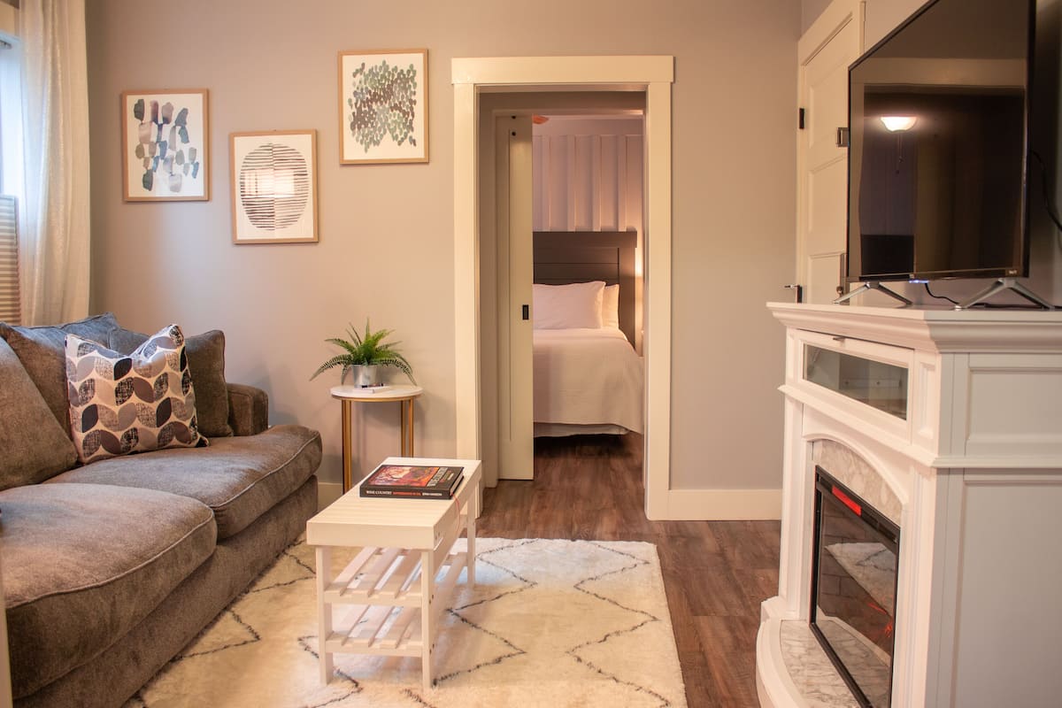 A living room with a sofa, a small table with a book, a potted plant, and a fireplace.
