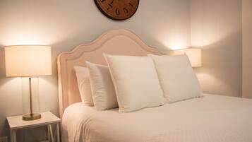 A neatly made bed with a headboard, two bedside lamps, and a wall clock.