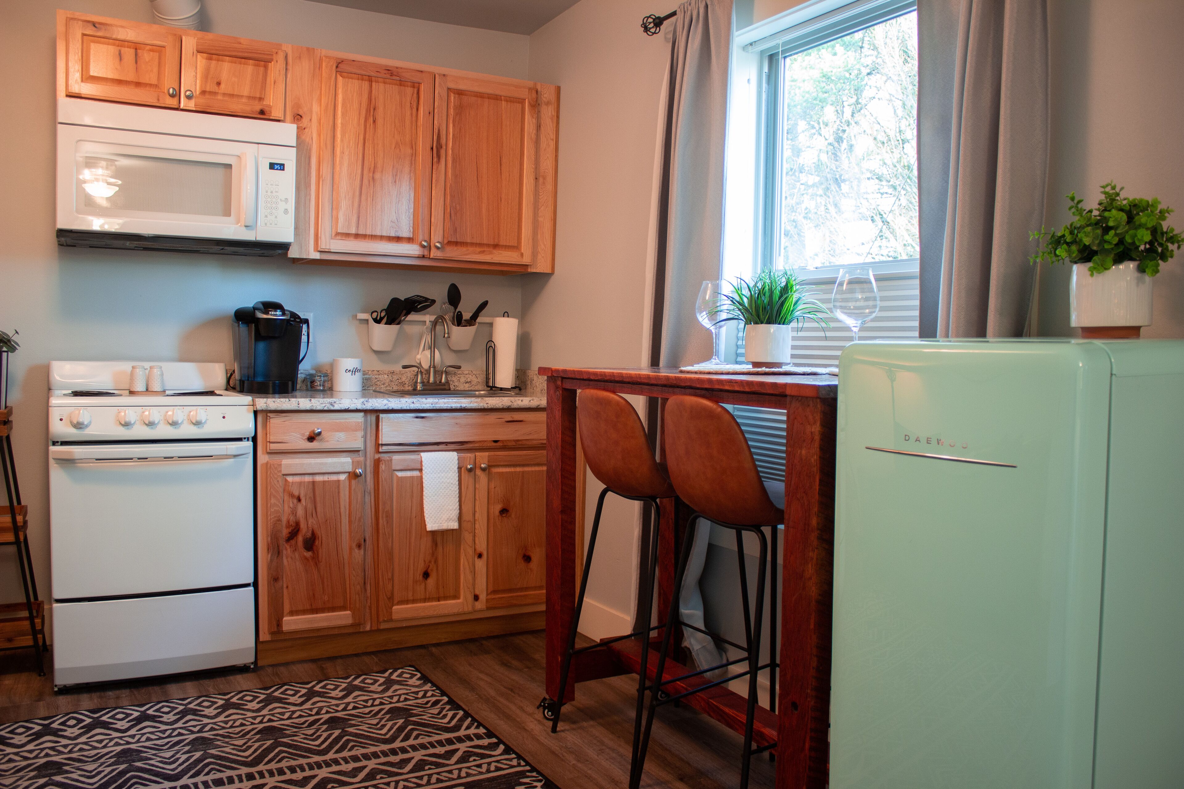 A kitchen with wooden cabinets, a white stove, a refrigerator, and a window with curtains.