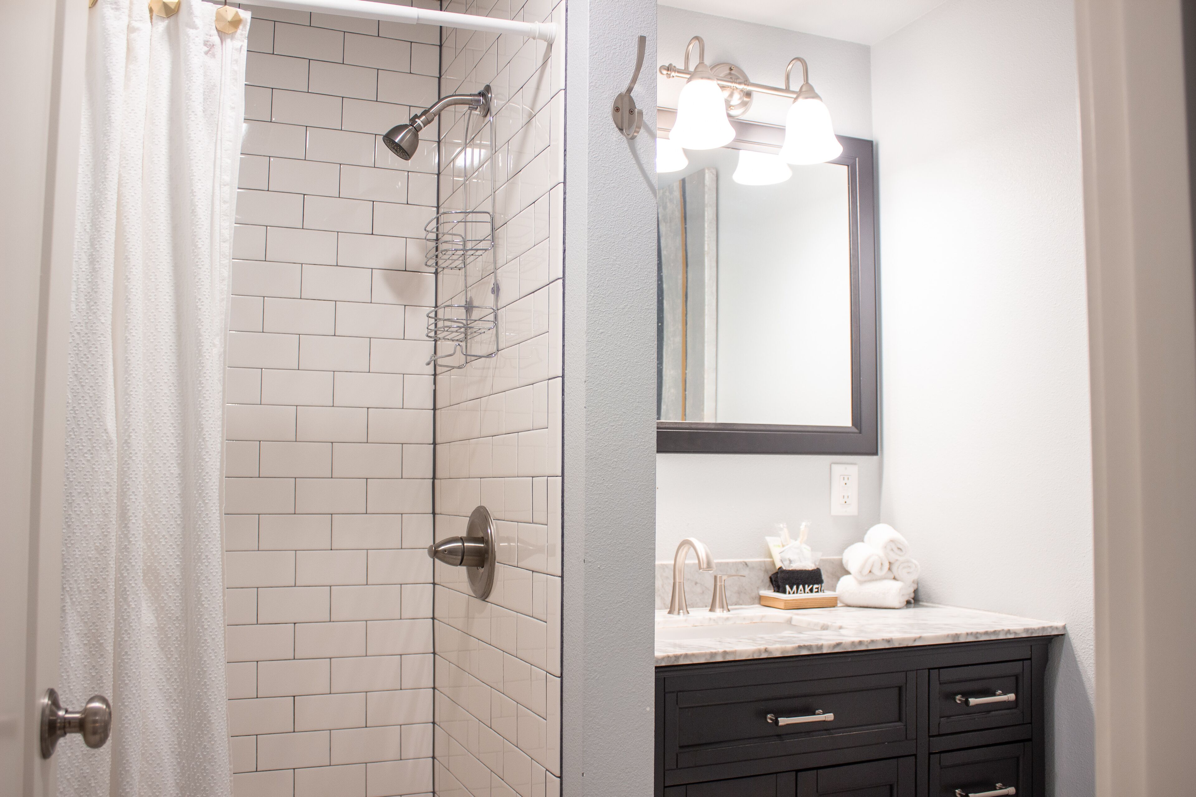 A bathroom with white tiled walls, a shower with a glass door, a sink with a mirror, and a towel rack.