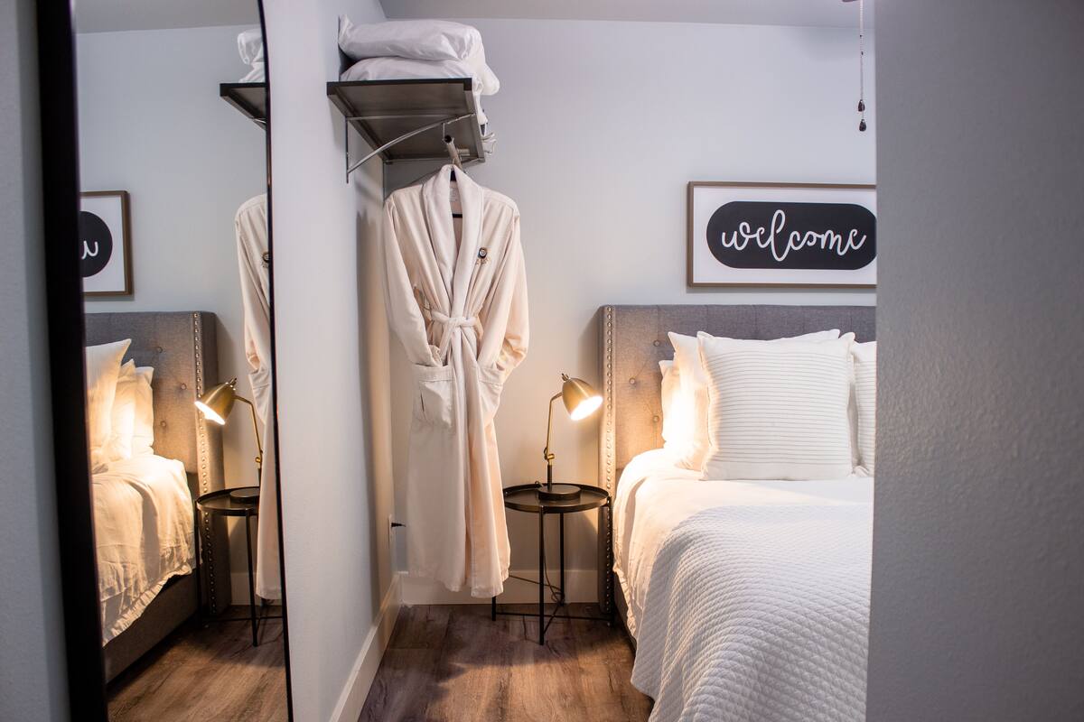 A hotel room with a bed, bedside tables, a robe hanging on a rack, and a welcome sign on the wall.