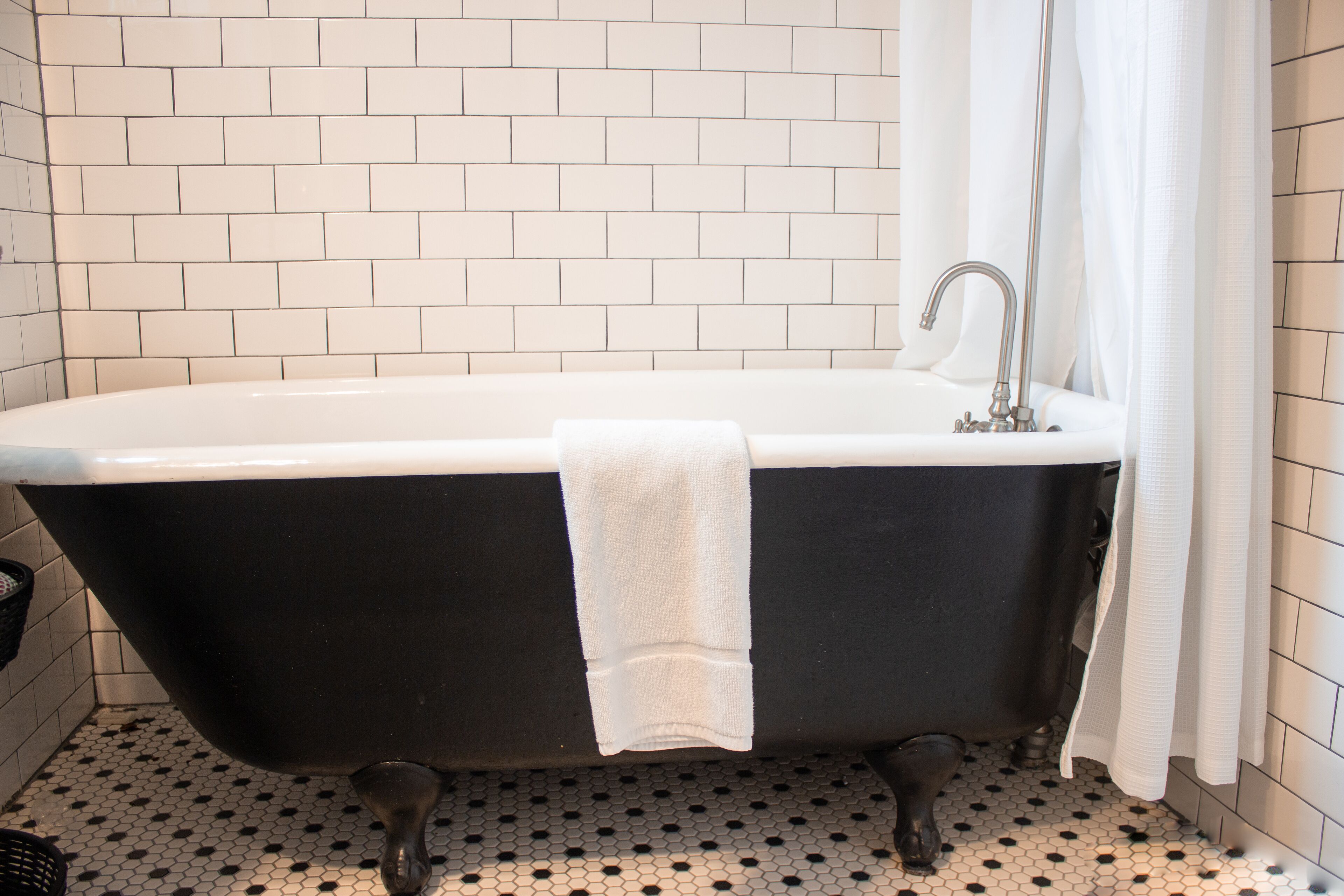 A black bathtub with a white towel, a white sink, and a white shower curtain in a bathroom with white tiled walls and floor.