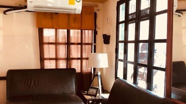 A room with a black leather sofa, a small table with a lamp, a decorative vase, and a window with blinds. - Hotel Ulúa (Veracruz)