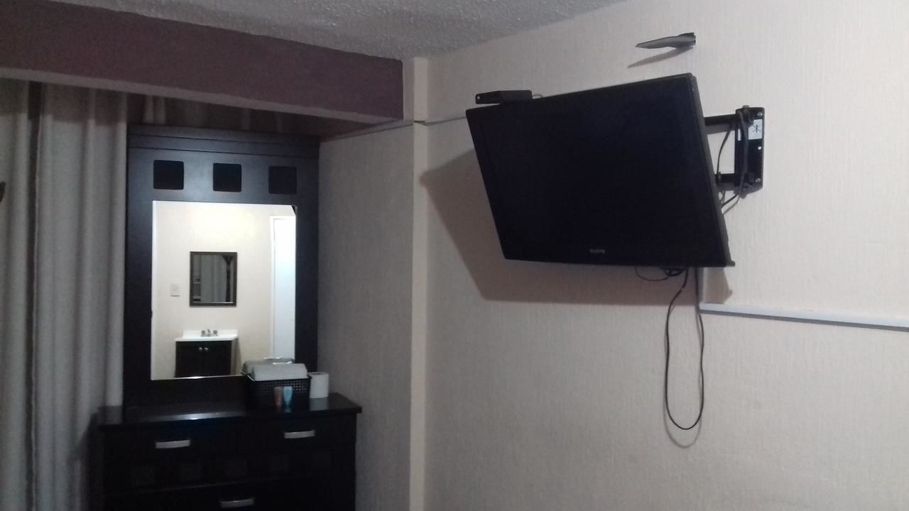 A room with a flat-screen TV mounted on the wall, a dresser with a mirror, and a small table with a cup.