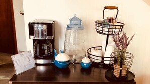A wooden cabinet with a coffee maker, a water dispenser, and a metal basket with books and a vase with flowers. - Hotel Ulúa (Veracruz)