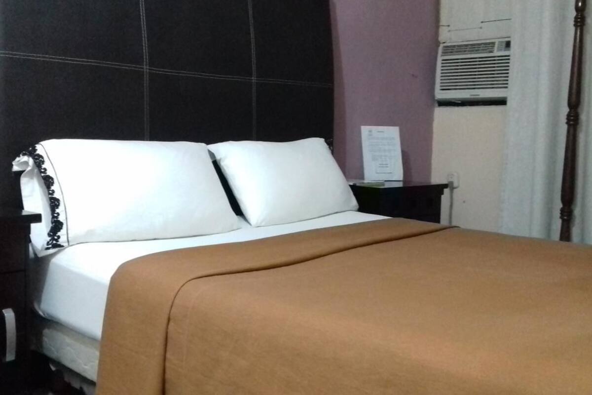 Ein Bett mit weißen Leinentüchern, einer braunen Decke und einem Kopfteil mit einer schwarzen Platte.