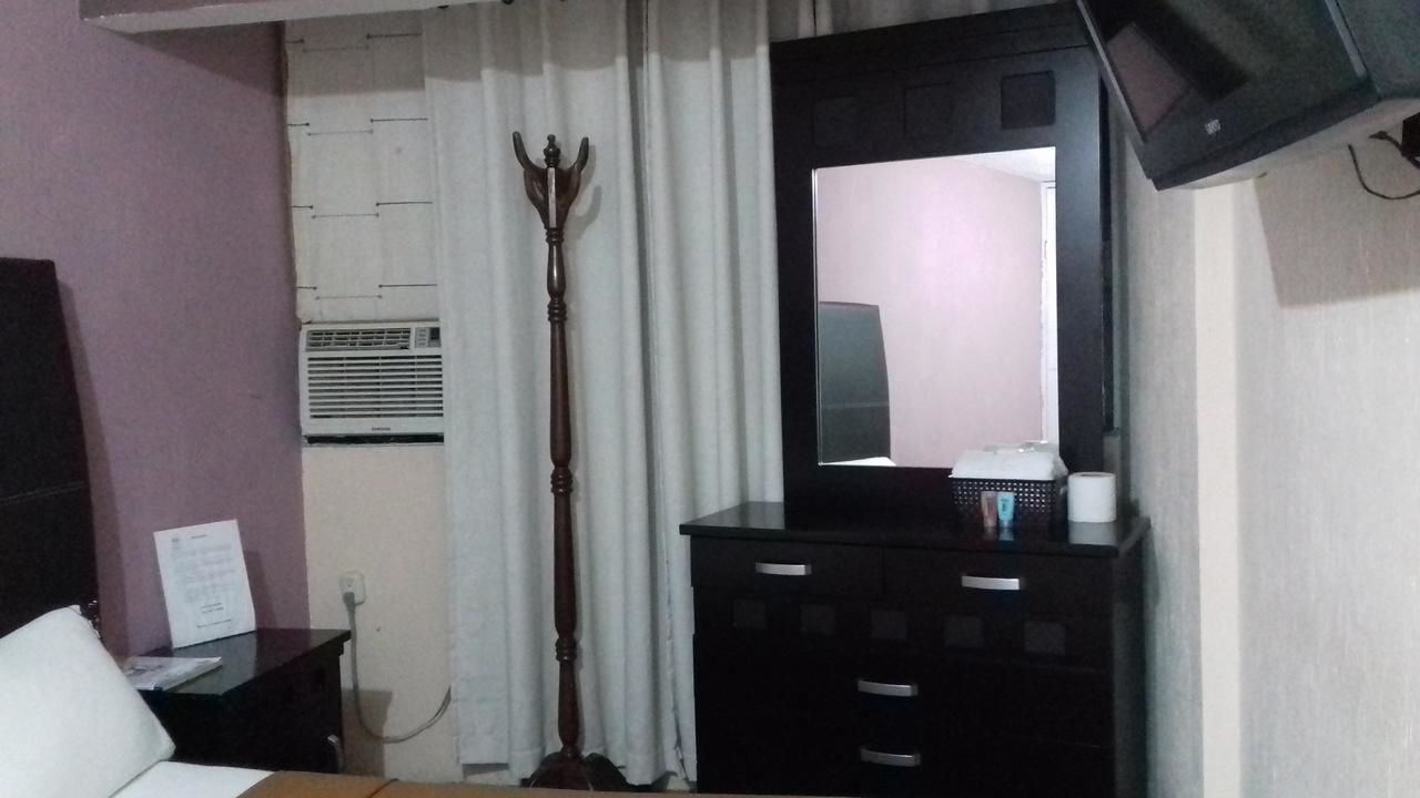 Habitación de hotel con cama, cómoda, espejo, televisor y equipo de aire acondicionado.
