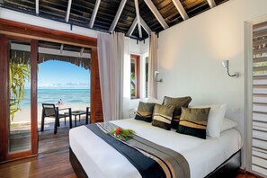 A bedroom with a bed, a nightstand, a window with curtains, and a view of the beach. - Moorea Beach Lodge (Moorea-Maiao)
