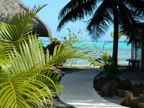 A pathway leading to a beach with palm trees and a thatched structure. - Moorea Beach Lodge (Moorea-Maiao)