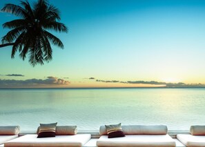 A beach view with a palm tree, a sunset, and lounge chairs with pillows. - Moorea Beach Lodge (Moorea-Maiao)