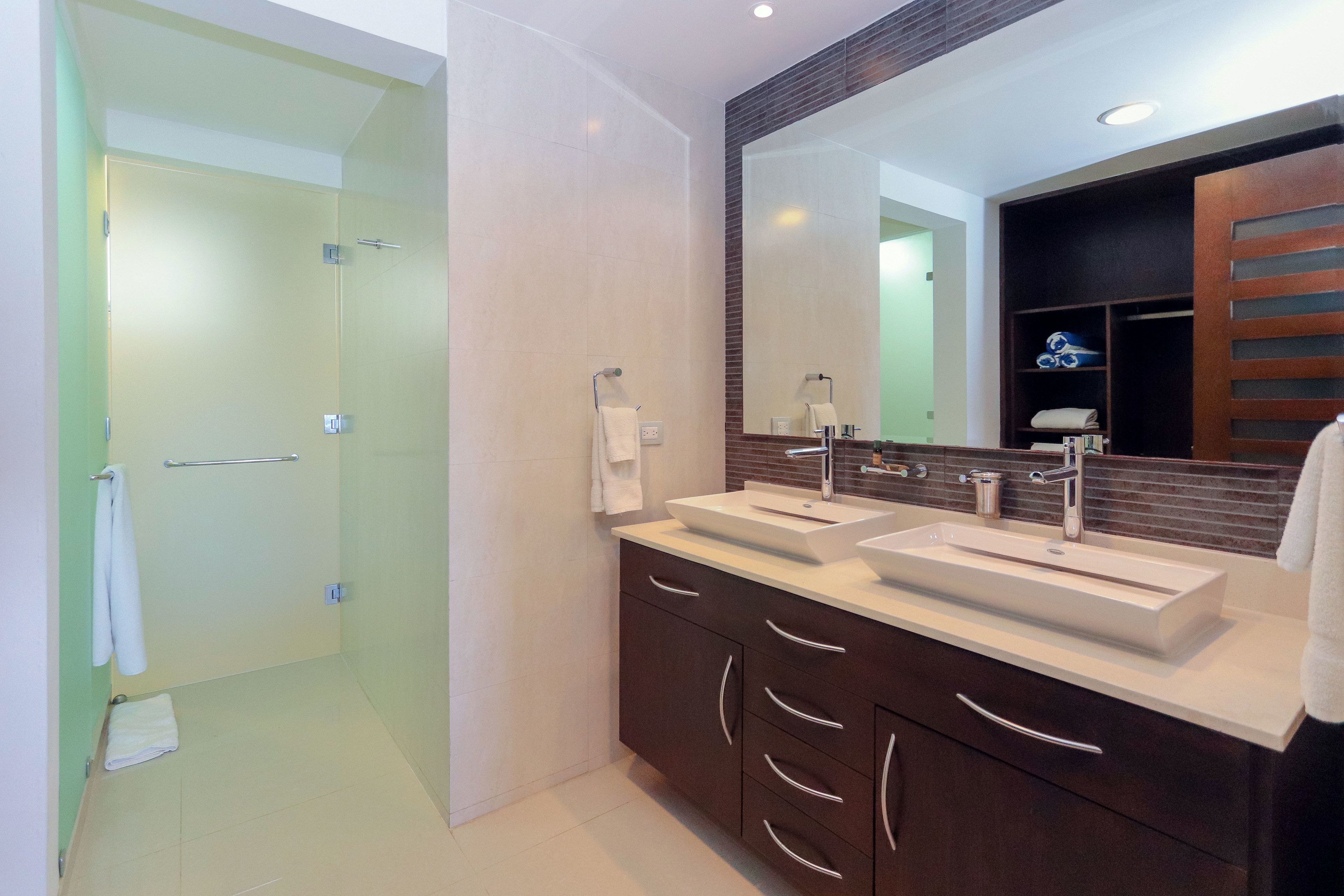 Une salle de bain moderne avec deux lavabos, un grand miroir et une douche à l’italienne.