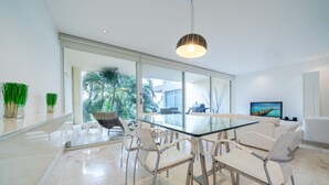 Un comedor moderno con una mesa y sillas de vidrio, ventanas amplias y vistas a palmeras.