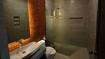 Un baño moderno con un espejo grande, un lavabo blanco, un inodoro y una zona de ducha con mampara de cristal.