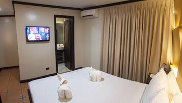 A hotel room with a bed, a television, an air conditioning unit, and a bathroom door.