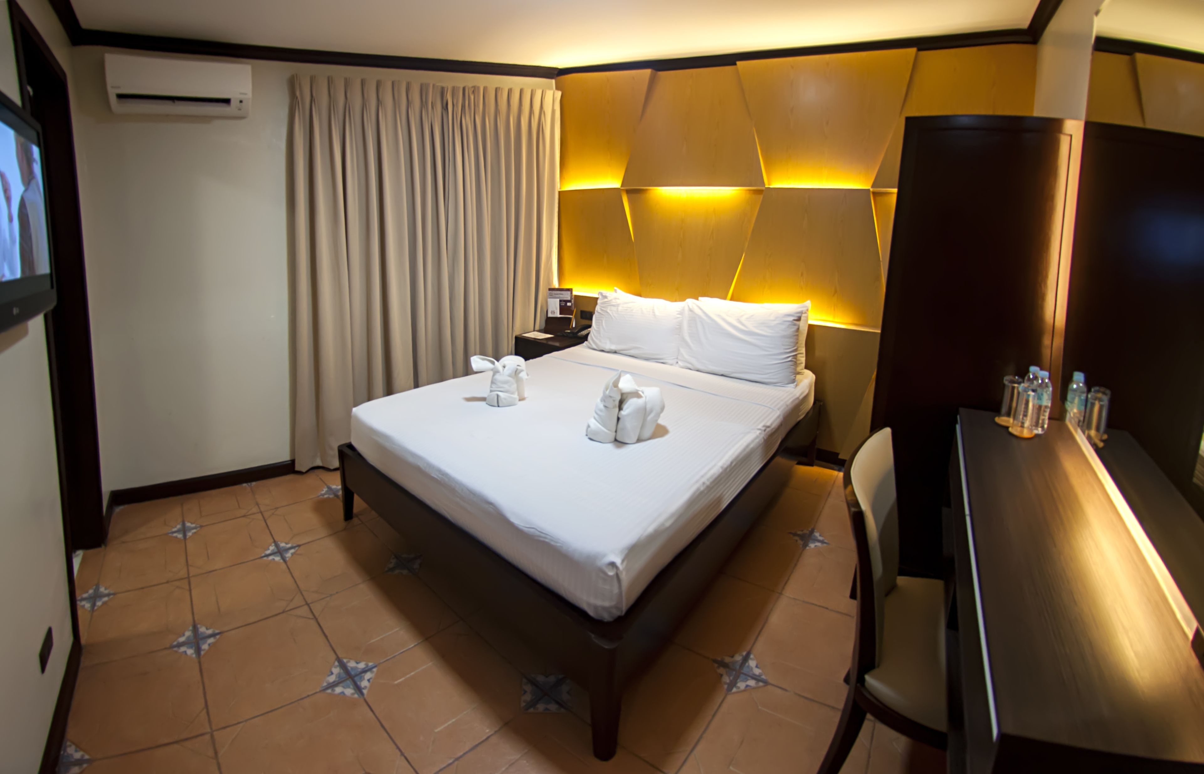Une chambre d’hôtel équipée d’un lit, d’un bureau, d’une chaise, d’une télévision, d’un climatiseur et de rideaux.