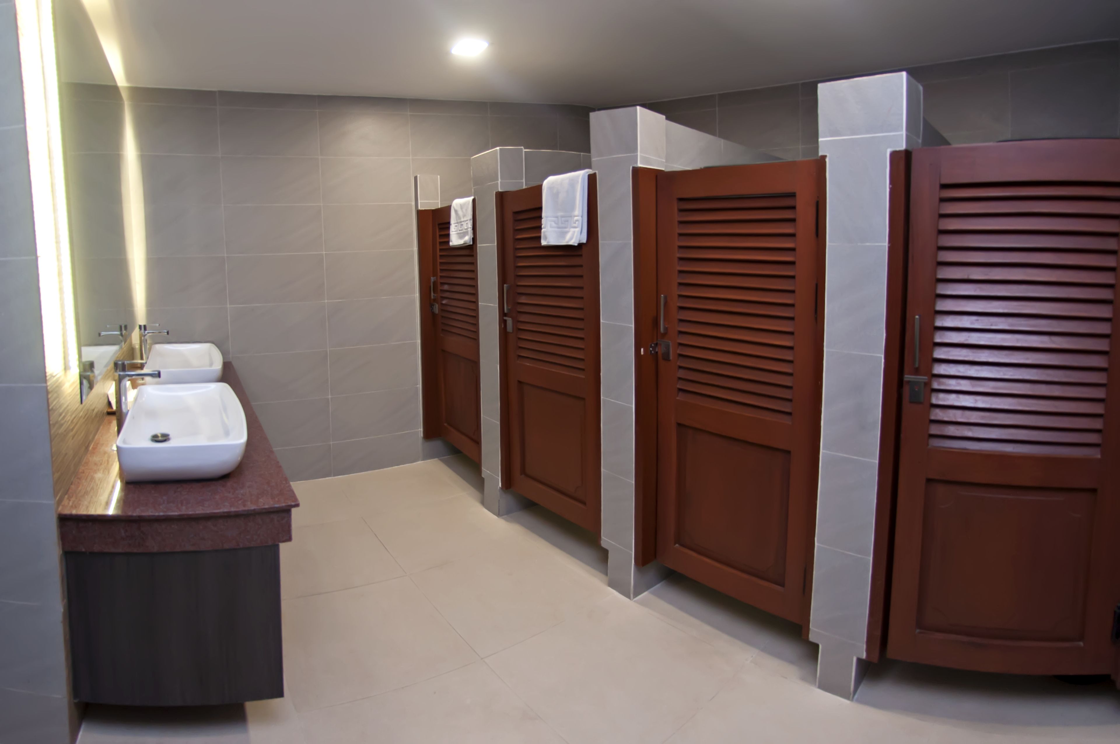 Un baño moderno con tres cabinas de madera, un lavabo y un espejo.