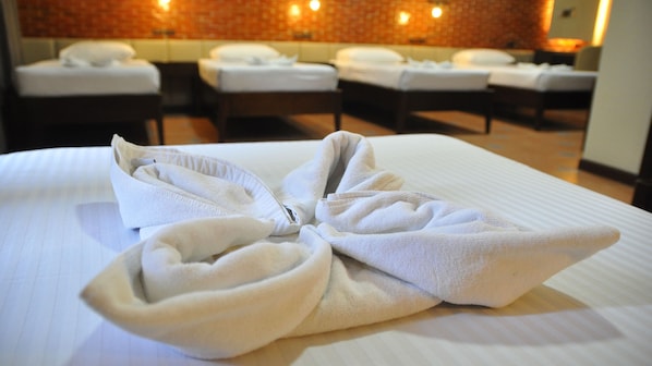 A hotel room with neatly folded towels on the bed and a brick wall with lights in the background.