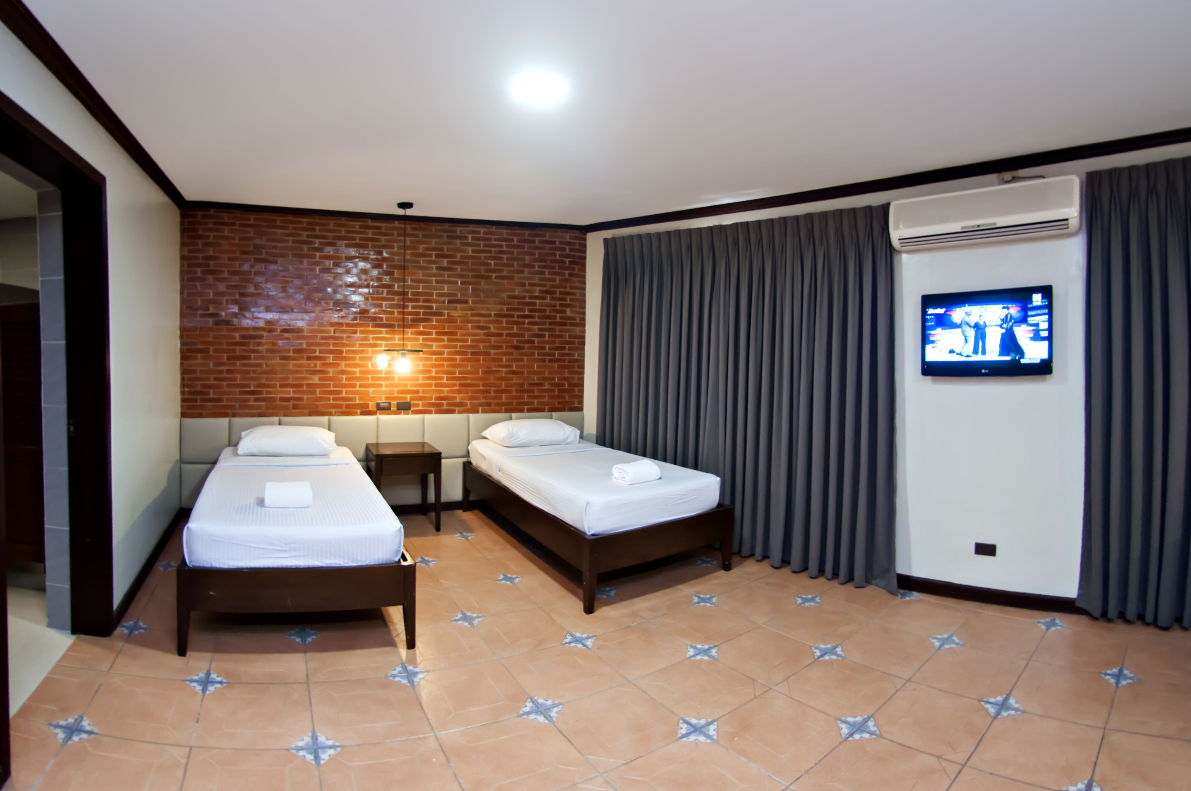 Una habitación de hotel con dos camas individuales, un televisor en la pared y una pared de ladrillo decorativa.