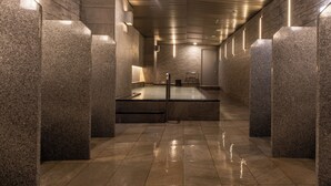 Un baño público moderno y bien iluminado, con pilares de granito, un lavamanos central y suelo de baldosas.