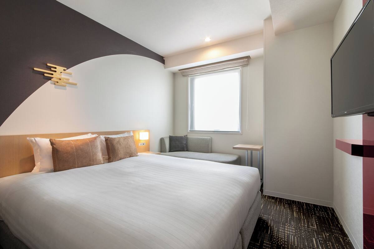 Habitación de hotel con una cama grande, un televisor de pantalla plana, una ventana con persianas y una mesita.