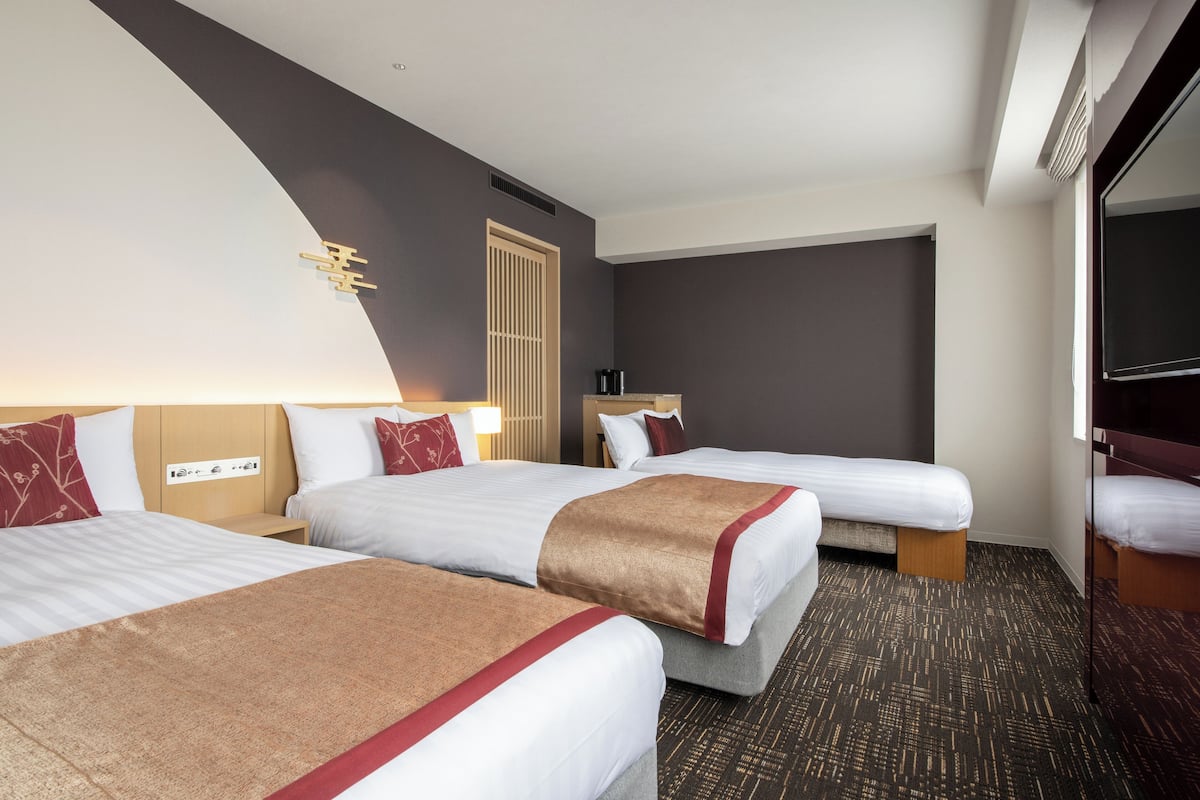 Habitación de hotel con tres camas, un ventanal grande y un televisor de pantalla plana.