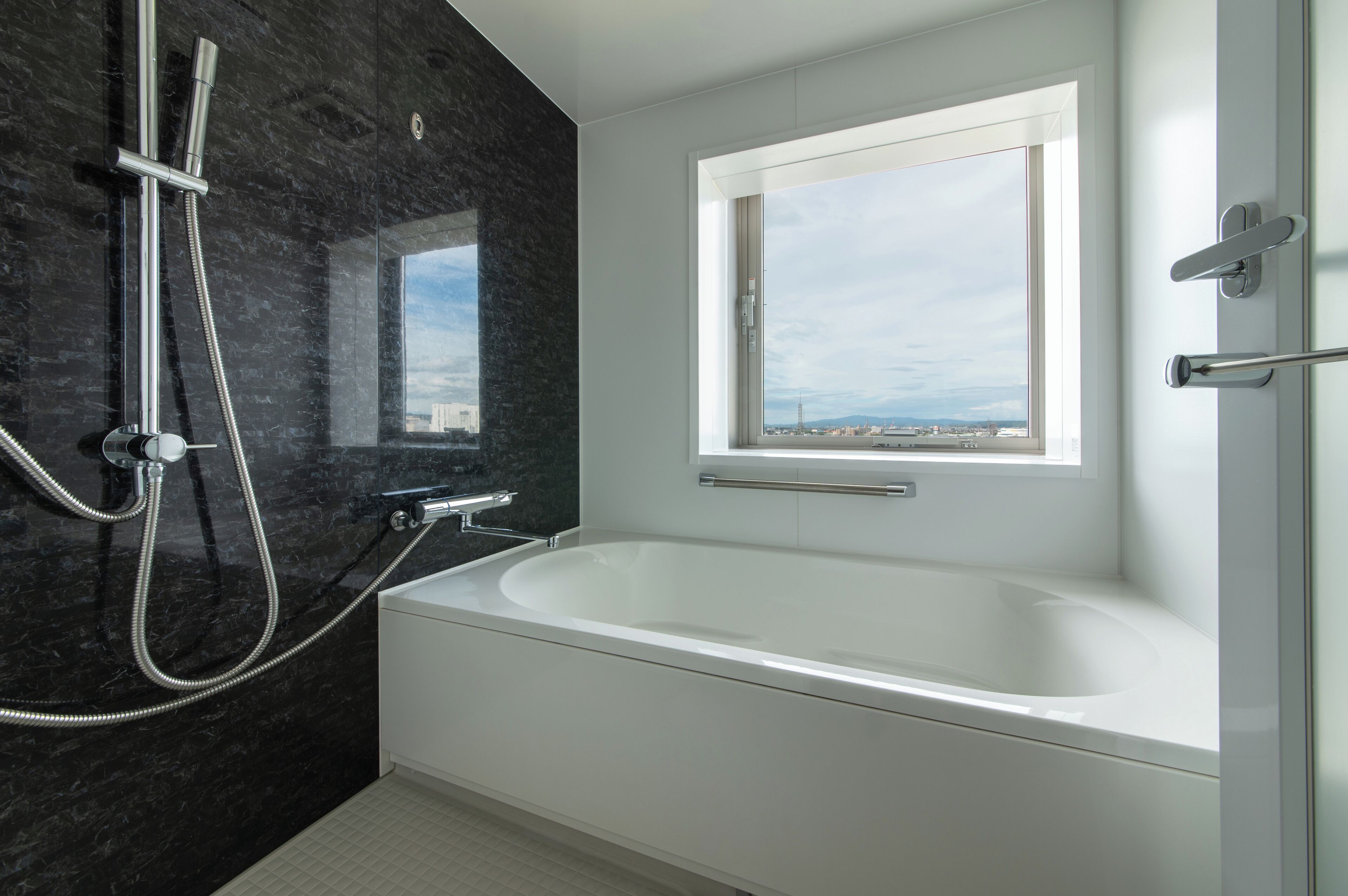 A modern bathroom with a large bathtub, a shower, and a window providing a view of the cityscape.