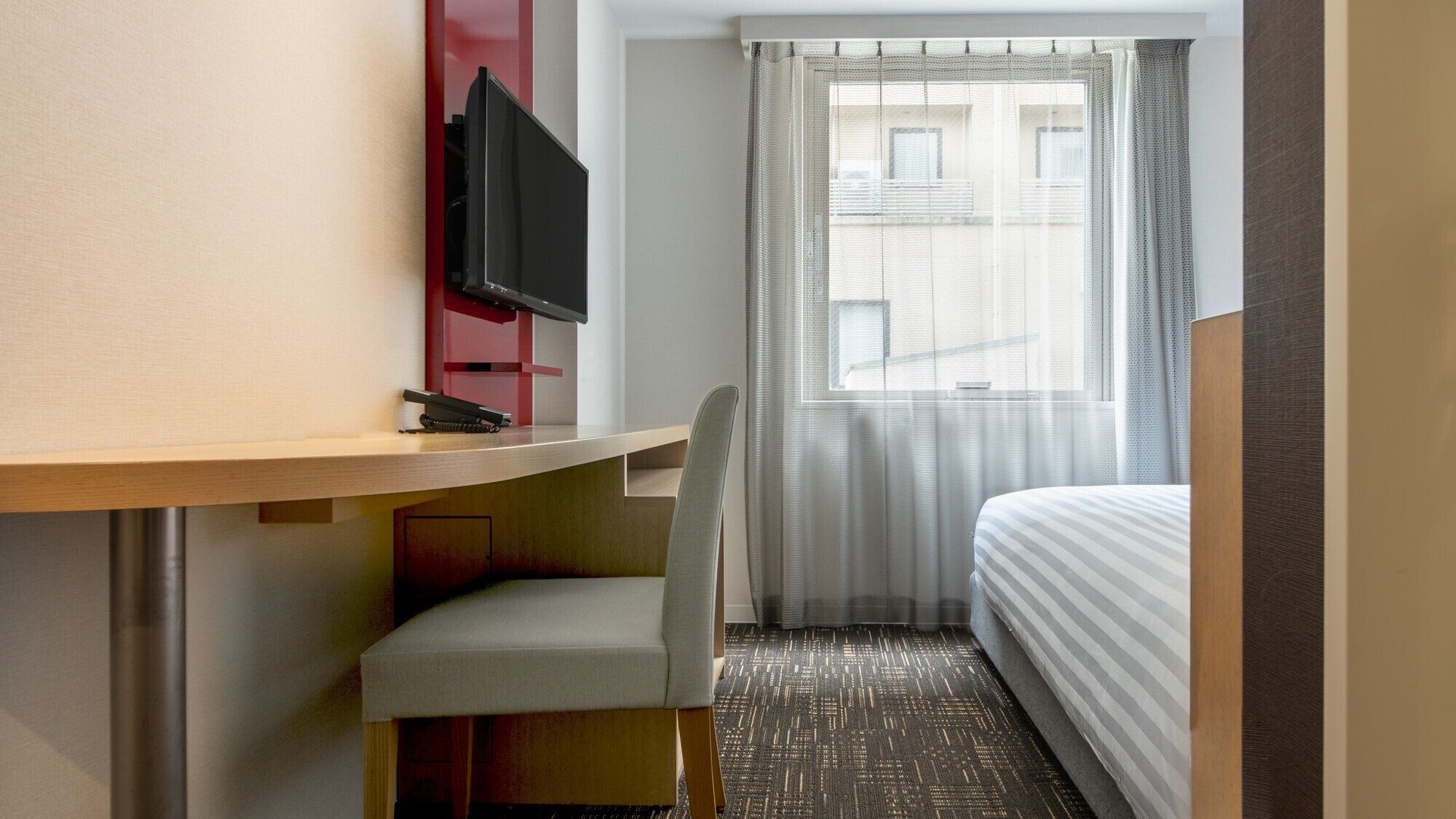 A hotel room with a desk, chair, TV, and a bed.