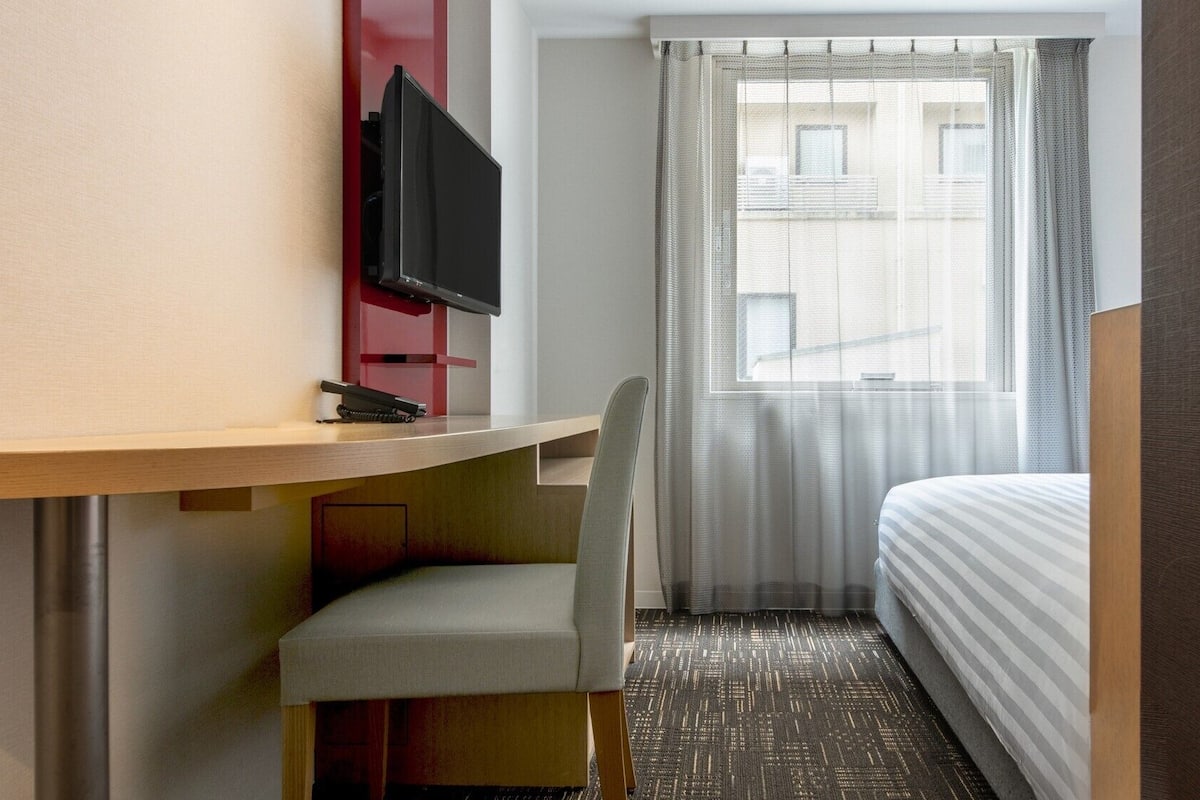 Habitación de hotel con escritorio, silla, televisor y cama.