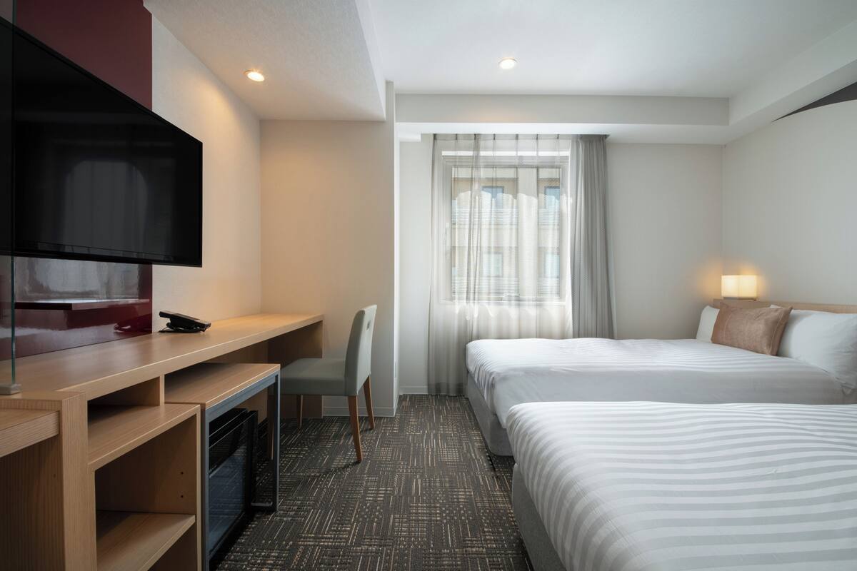Habitación de hotel con dos camas, un escritorio, un televisor y una ventana con cortinas.