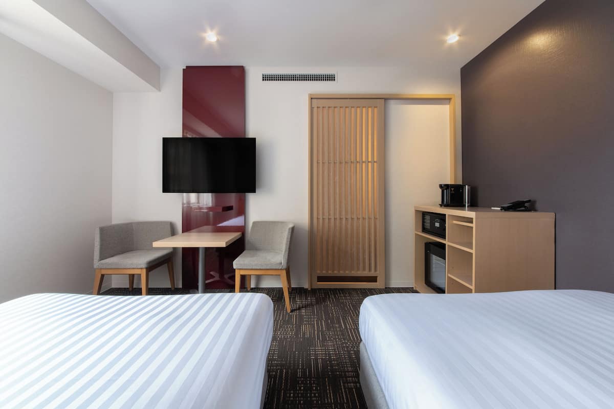 Habitación de hotel con dos camas, un escritorio, una silla, televisor, armario y cafetera.