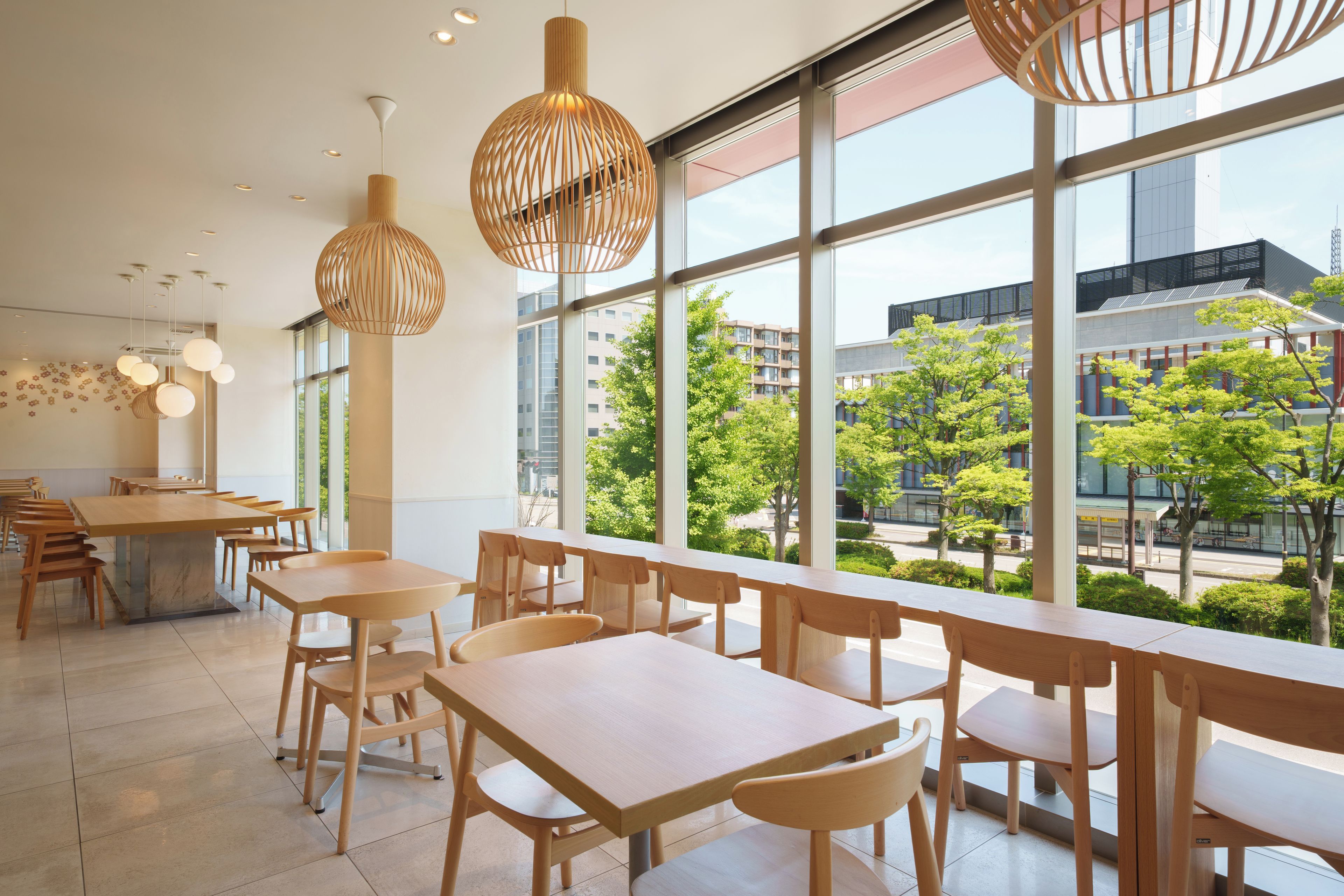 A modern dining area with wooden tables and chairs, large windows offering a view of the cityscape.