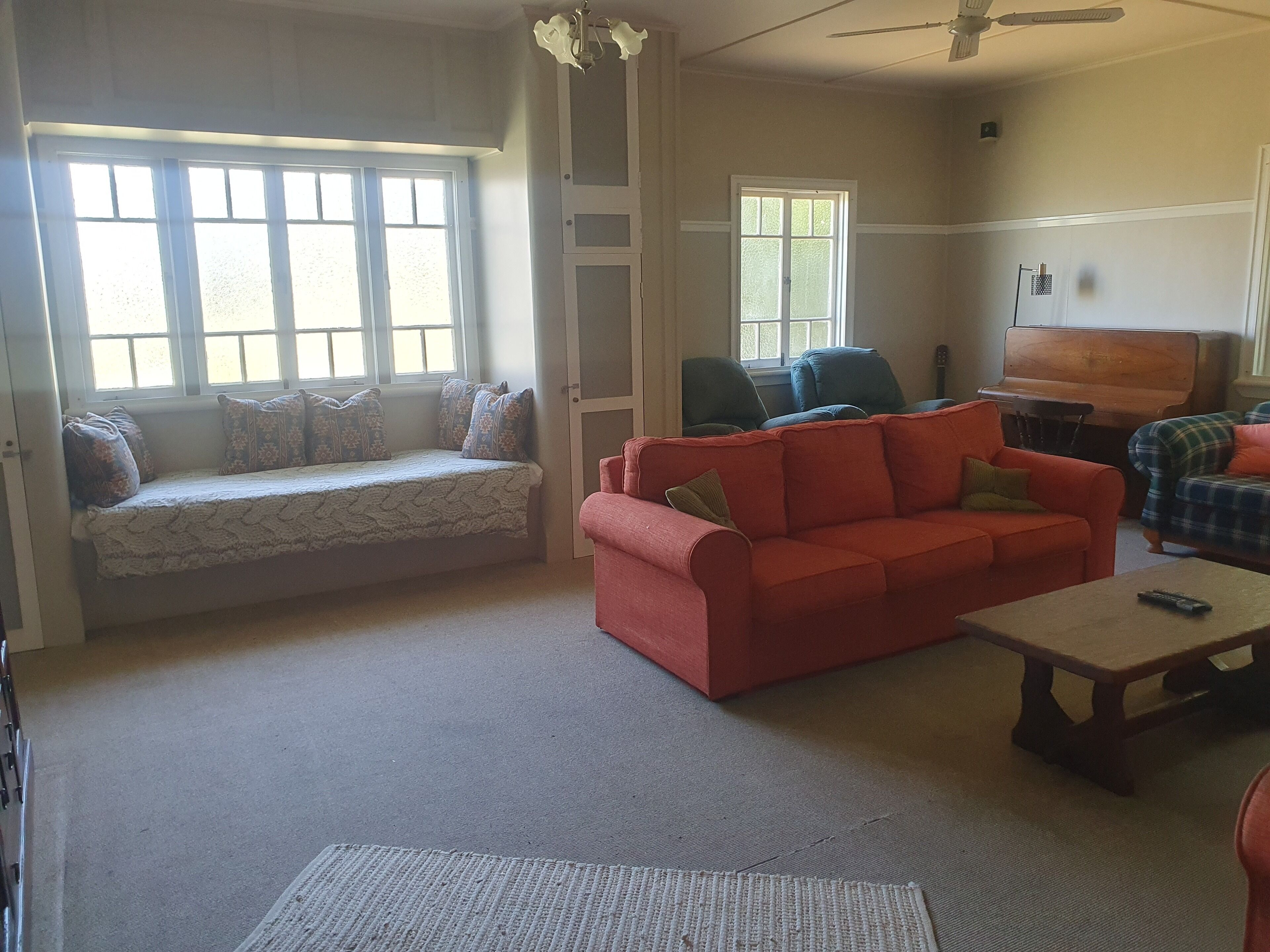 Una sala de estar con un sofá, un sillón rojo, una mesa de centro de madera y un banco junto a la ventana.
