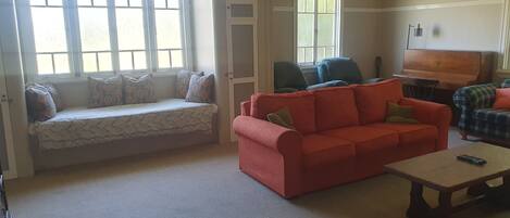 Una sala de estar con un sofá, un sillón rojo, una mesa de centro de madera y un banco junto a la ventana.