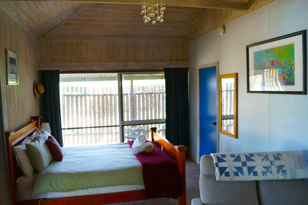A bedroom with a bed, a chair, a window, and a painting on the wall.