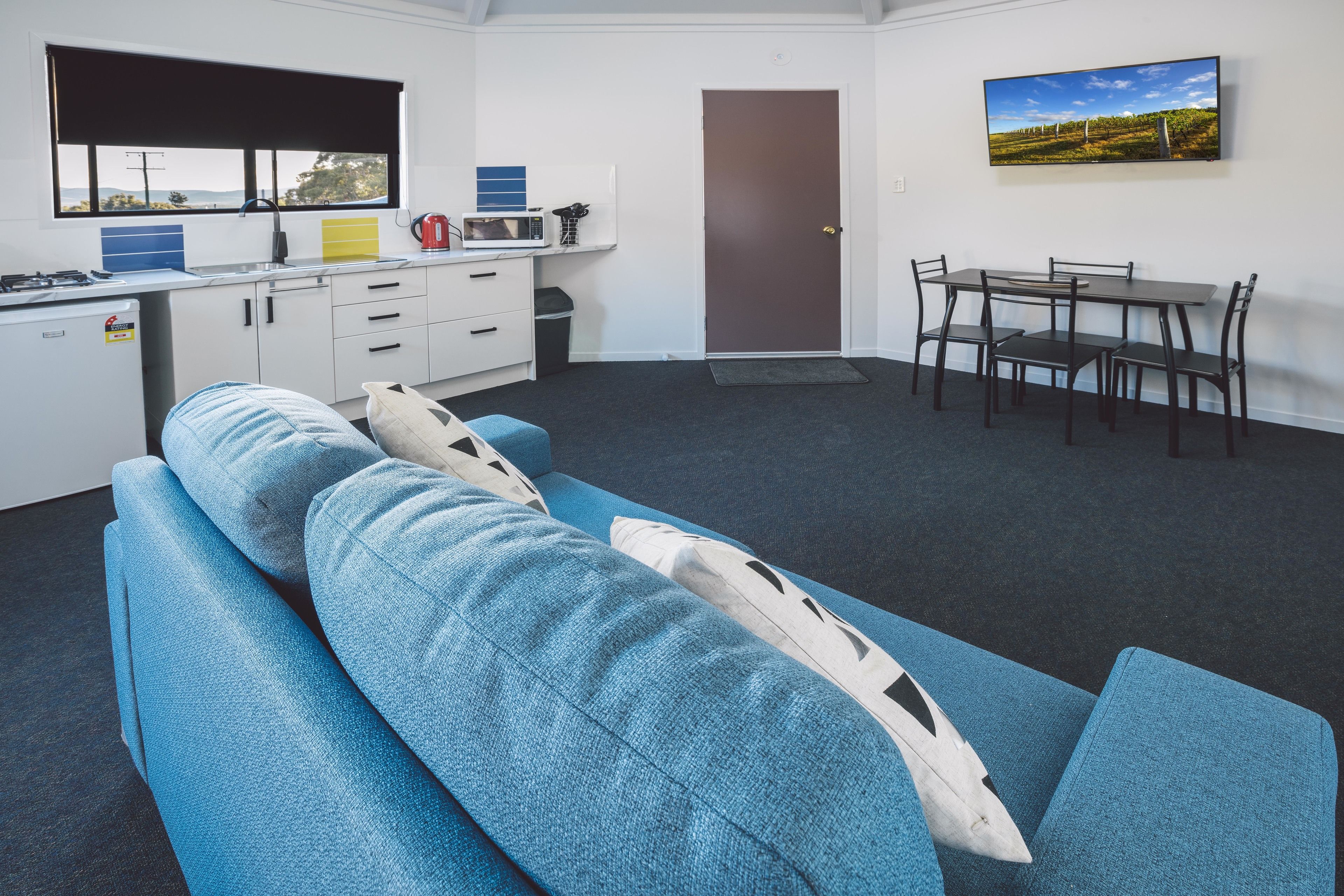 Ein modernes Zimmer mit einem blauen Sofa, einem Esstisch mit Stühlen, einer Küchenzeile und einer Tür.