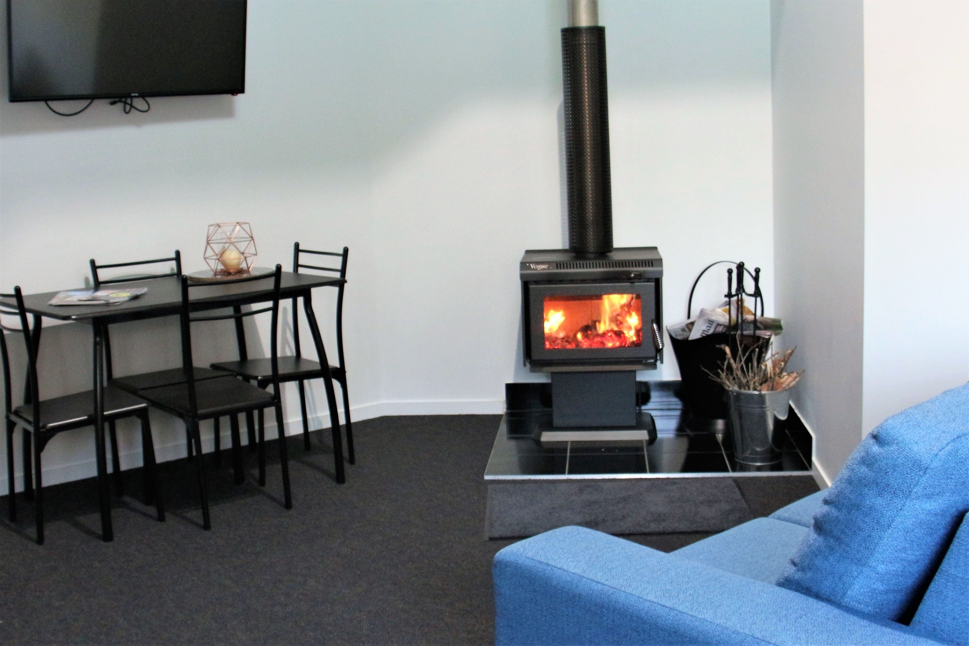 A living room with a black sofa, a dining table with chairs, and a wood-burning stove.