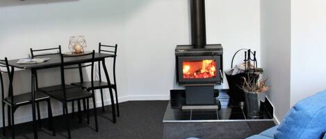 A living room with a black sofa, a dining table with chairs, and a wood-burning stove.