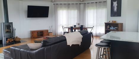 A modern living room with a black leather sofa, a wooden dining table, and a kitchen area with a bar stool.