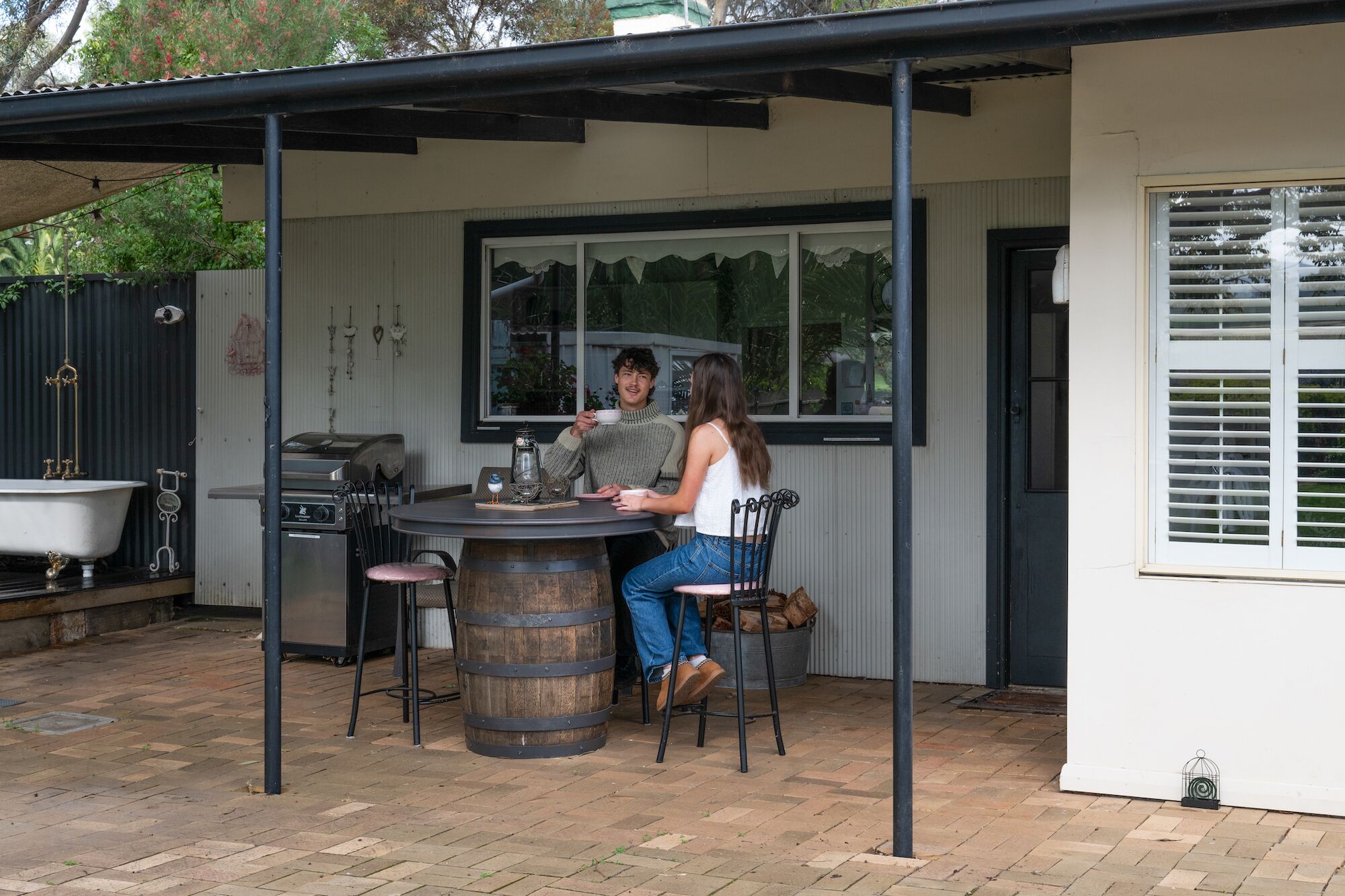 Un espacio cubierto para comer al aire libre con mesa, sillas, una parrilla y un barril rústico.