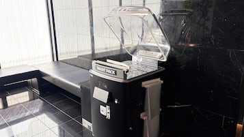 Una máquina expendedora de café con una cubierta protectora transparente, una etiqueta que dice 'SMART PACK' y un pequeño contenedor de basura adherido.