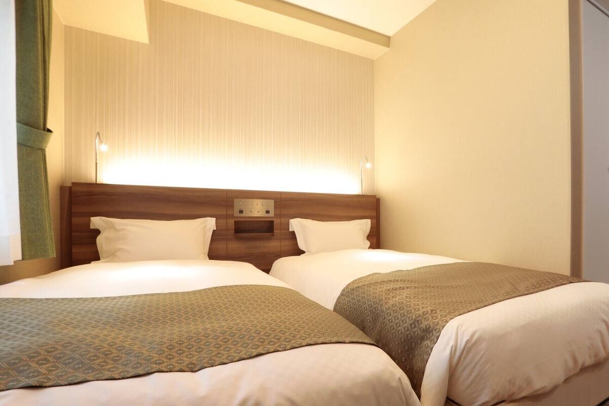 A hotel room with two beds, a wooden headboard, a wall-mounted light, and a door.
