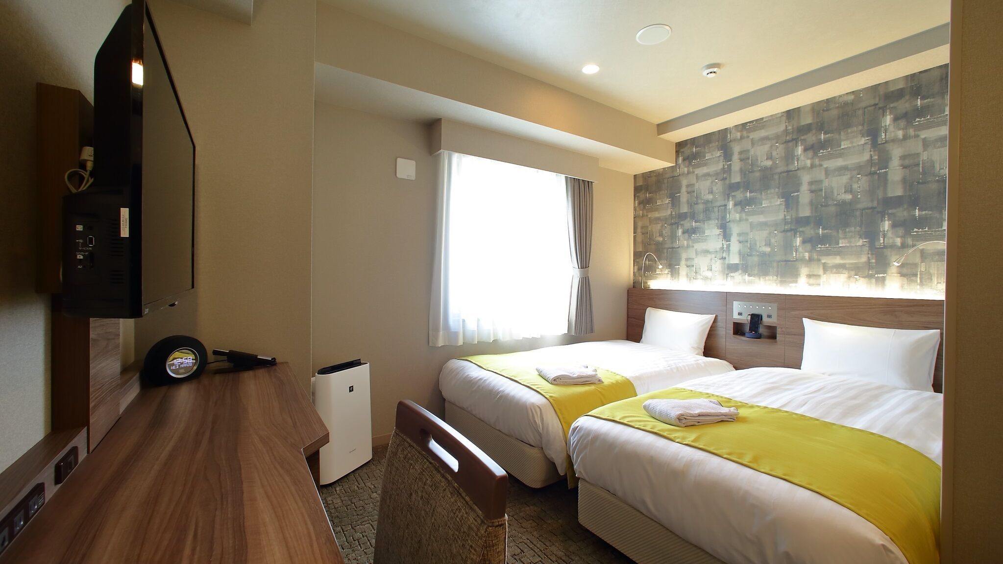 Habitación de hotel con dos camas, un escritorio, televisor y vistas a la ciudad.